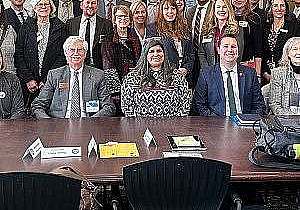 Large group photo of Hike the Hill participants lined up in rows behind a large conference table