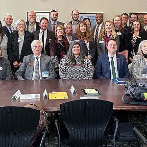 Large group photo of Hike the Hill participants lined up in rows behind a large conference table