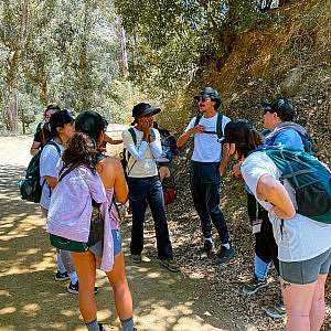 A diverse group of participants smile while they circle up in a shady section of the trail