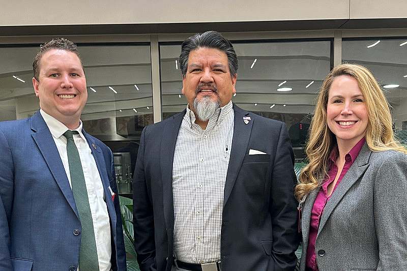 Three people in business attire smile or a photo.